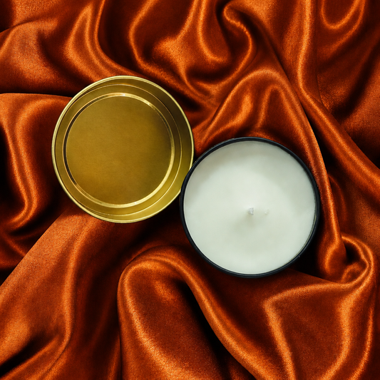 An open candle tin with white wax and a gold-toned lid, placed on draped orange satin fabric.